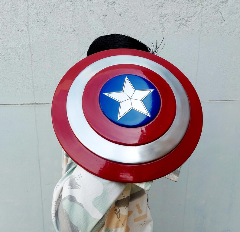 May include: A circular shield in red, white, and blue, featuring a star emblem. The shield has a glossy finish. The centre has a blue circle with a white star. The outer ring is red, and the middle ring is silver.