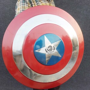 Op de afbeelding: Een rood, wit en blauw Captain America schild met een zilveren metalen rand. Het schild heeft een vijfpuntige ster in het midden met een blauwe achtergrond en een zilveren drakenlogo met de tekst "Coastal" eronder.
