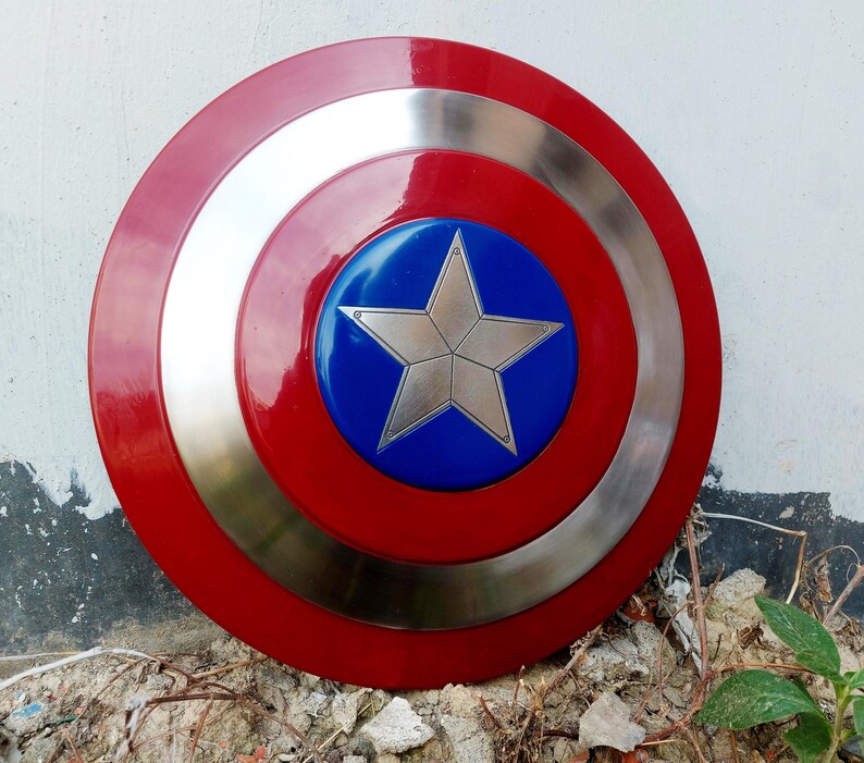 May include: A circular shield in red, silver, and blue. The centre features a silver star on a blue background, encircled by a silver band. The outer edge is red, creating a striking design.