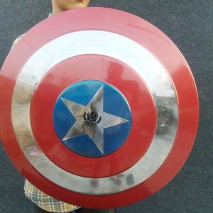 Op de afbeelding: Een rood, wit en blauw Captain America schild met een zilveren ster in het midden. Het schild heeft een zilveren rand en is gemaakt van metaal.