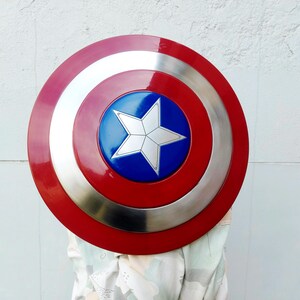 May include: A circular shield featuring a red border, a silver band, and a blue central disc with a white star. This shield is a replica of Captain America's shield, a well-known superhero accessory.