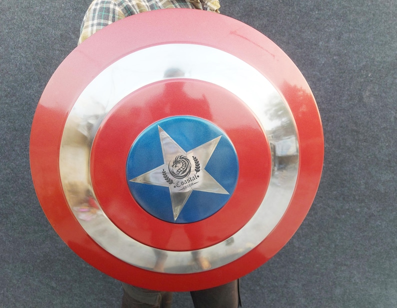 Op de afbeelding: Een rood, wit en blauw Captain America schild met een zilveren metalen rand. Het schild heeft een vijfpuntige ster in het midden met een drakenlogo en de tekst "Coastal", "Decor" en "com".