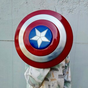 May include: A circular shield in red, white, and blue. The shield features a red outer ring, a silver central section, and a blue centre with a white star. This shield is a replica of Captain America's shield.