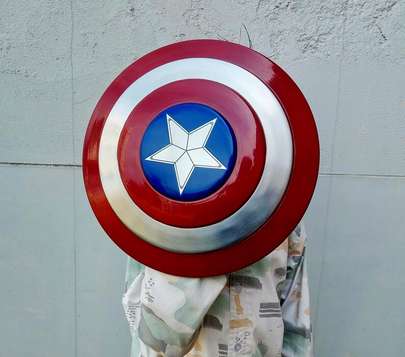 May include: A circular shield in red, white, and blue. The shield features a red outer ring, a silver central section, and a blue centre with a white star. This shield is a replica of Captain America's shield.