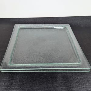 May include: A rectangular clear glass tray featuring a textured, pebbled surface on the interior base and a smooth, raised border frame. The glass has a slight green tint along the edges, showcasing a simple, functional design for serving.