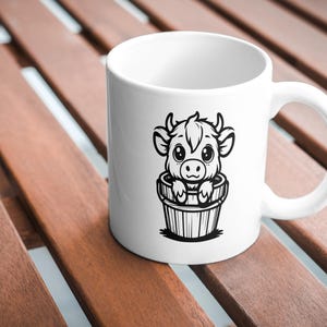 Puede incluir: Taza de cer&aacute;mica blanca con una ilustraci&oacute;n en blanco y negro de una vaca de dibujos animados en un cubo. La vaca tiene ojos grandes y mira al espectador.