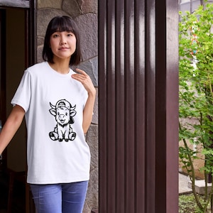 Puede incluir: Camiseta blanca con una ilustraci&oacute;n en blanco y negro de un ternero de dibujos animados con una gorra de b&eacute;isbol.