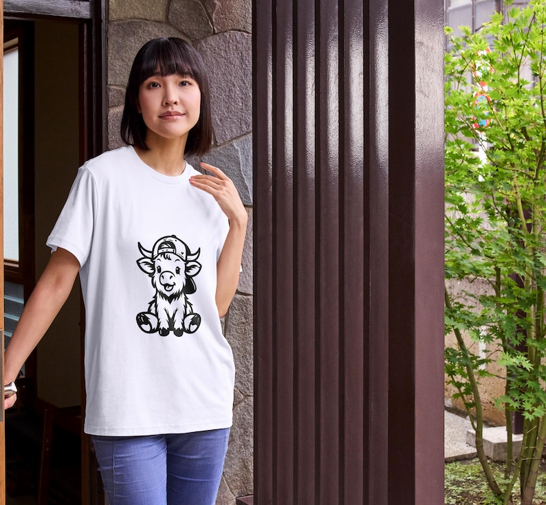 Puede incluir: Camiseta blanca con una ilustraci&oacute;n en blanco y negro de un ternero de dibujos animados con una gorra de b&eacute;isbol.