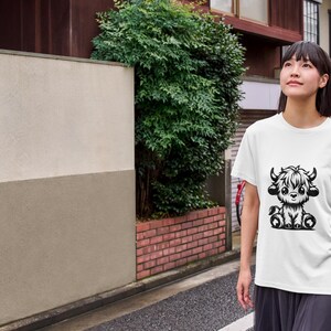 Puede incluir: Una camiseta blanca con una ilustraci&oacute;n en blanco y negro de una vaca Highland linda y de dibujos animados. La vaca est&aacute; sentada con las piernas cruzadas y tiene una melena esponjosa.