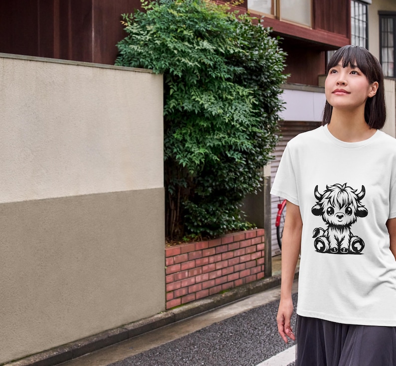 Puede incluir: Una camiseta blanca con una ilustraci&oacute;n en blanco y negro de una vaca Highland linda y de dibujos animados. La vaca est&aacute; sentada con las piernas cruzadas y tiene una melena esponjosa.