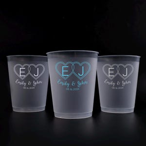 May include: Three frosted plastic cups with a dark rim. Each cup features a heart design with the initials "E" and "J", the names "Emily & John", and the date "08.16.2026". The design is white or light blue.