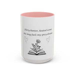 Puede incluir: Taza de cerámica blanca con interior rosa. La taza presenta el texto "Flirty banter, heated scenes, this mug fuels my spicy dreams" con una ilustración floral y dos garabatos de corazón. Un regalo perfecto para los amantes de los libros.