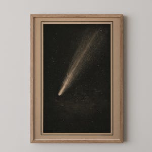 May include: A framed wall art print featuring a detailed illustration of a comet streaking across a dark, star-filled night sky. The artwork is encased in a light-toned wooden frame with a tan mat border, presenting a celestial scene in monochrome.