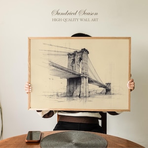 Könnte beinhalten: Ein gerahmter Druck mit einer detaillierten Skizze der Brooklyn Bridge. Das Kunstwerk ist in Schwarzweiß gehalten, wobei die architektonischen Details der Brücke hervorgehoben werden. Der Rahmen besteht aus hellem Holz. Der Text "Sundried Season HIGH QUALITY WALL ART" steht oben.