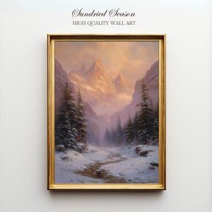 Może przedstawiać: Oprawiony obraz krajobrazu zaśnieżonej górskiej doliny. Grafika ma złotą ramę i tekst "Sundried Season HIGH QUALITY WALL ART". Obraz przedstawia ośnieżone drzewa i góry pod ciepłym, złotym niebem.