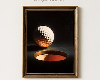 Op de afbeelding: Ingelijste wandkunst met een golfbal in de buurt van een hole. De golfbal is wit met putjes en heeft een bronzen schaduw. Het gat is donker met een rood-oranje binnenkant. De lijst heeft een donkere houtkleur. Tekst bovenaan luidt "Sundried Season" en "HIGH QUALITY WALL ART".