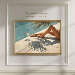 Pode incluir: Impressão artística emoldurada com uma cena à beira da piscina com um cocktail e pernas. A obra de arte tem uma moldura dourada e o texto "Sundried Season HIGH QUALITY WALL ART". A imagem mostra um copo de cocktail e a sombra de uma palmeira.