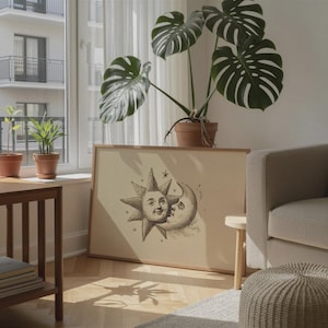 Könnte beinhalten: Ein rechteckiger gerahmter Druck mit einer schwarzen Tuschezeichnung von Sonne und zunehmendem Mond mit menschlichen Gesichtern auf cremefarbenem Hintergrund. Das Kunstwerk befindet sich in einem hellen Holzrahmen und steht auf einem Holzboden.