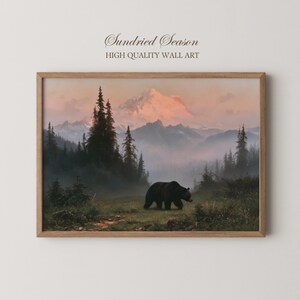 May include: A framed wall art print titled Sundried Season High Quality Wall Art featuring a landscape painting of a black bear walking through a misty meadow with tall evergreen trees and snow-capped mountains under a soft pink sunset sky.