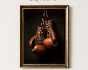 Pode incluir: Uma impressão emoldurada com um par de luvas de boxe de couro marrom vintage penduradas contra um fundo escuro. As luvas são amarradas e suspensas por cordas finas. A obra de arte é rotulada como "Sundried Season HIGH QUALITY WALL ART".