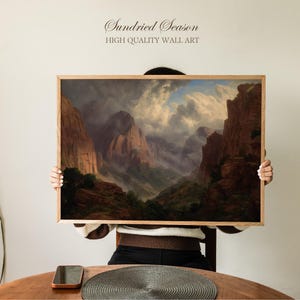 Puede incluir: Una pintura de paisaje enmarcada que representa una cordillera bajo un cielo nublado. La obra de arte tiene una estética vintage con tonos cálidos y un marco de madera. El texto "Sundried Season HIGH QUALITY WALL ART" está en la parte superior.