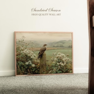 May include: A framed landscape print with a bird on a post, set against a backdrop of rolling hills and fields. The artwork uses a soft colour palette of greens, browns, and whites. The text at the top reads "Sundried Season" and "HIGH QUALITY WALL ART".