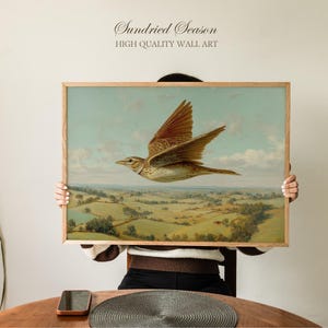 May include: A framed print of a bird in flight over a rural landscape. The artwork has a vintage style, with a light blue sky and a wooden frame. The text "Sundried Season HIGH QUALITY WALL ART" is at the top of the print.