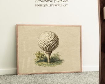 Op de afbeelding: Een ingelijste vintage illustratie van een golfbal op een tee. Het kunstwerk heeft een beige achtergrond met een golfbal in het midden, omringd door groen gebladerte. De tekst "Sundried Season" en "HIGH QUALITY WALL ART" staat bovenaan.