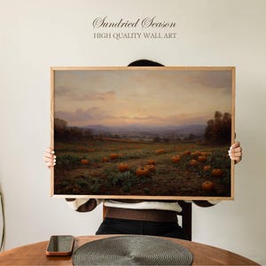 Può includere: Dipinto di paesaggio incorniciato con un campo di zucche al tramonto. L'opera d'arte ha una cornice in legno e il testo "Sundried Season HIGH QUALITY WALL ART" in alto. Il dipinto raffigura un campo di zucche con una catena montuosa sullo sfondo.