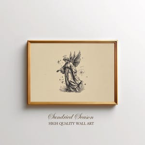 May include: A framed print with a black and white illustration of an angel with wings and a halo. The artwork is set against a beige background and framed in a gold-coloured frame. The text "Sundried Season HIGH QUALITY WALL ART" is at the bottom.