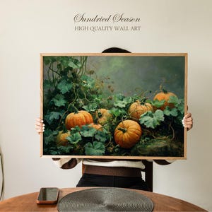 Op de afbeelding: Een ingelijste wandkunstprint met een stilleven van pompoenen en bladeren. Het kunstwerk heeft een warm kleurenpalet met oranje pompoenen en groene bladeren. De tekst "Sundried Season HIGH QUALITY WALL ART" staat bovenaan.