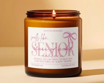 May include: A lit candle in an amber glass jar with a white label featuring a pink bow illustration and text that reads: Scented Remarks, smells like... SENIOR class of 2026, rebecca, INFUSED W/ THE LAST FIRSTS, THE BEST LASTS, & THE SWEET SMELL OF 'ALMOST' FREEDOM!, NET WEIGHT 9 OZ, NATURAL SOY WAX.