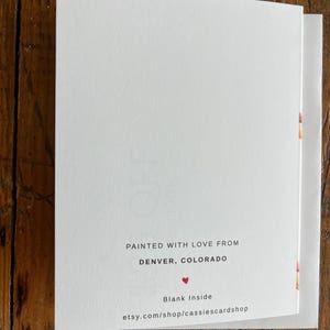 May include: A white greeting card with black text that reads: PAINTED WITH LOVE FROM DENVER, COLORADO, a small red heart icon, the text Blank Inside, and the website address etsy.com/shop/cassiescardshop printed at the bottom center.
