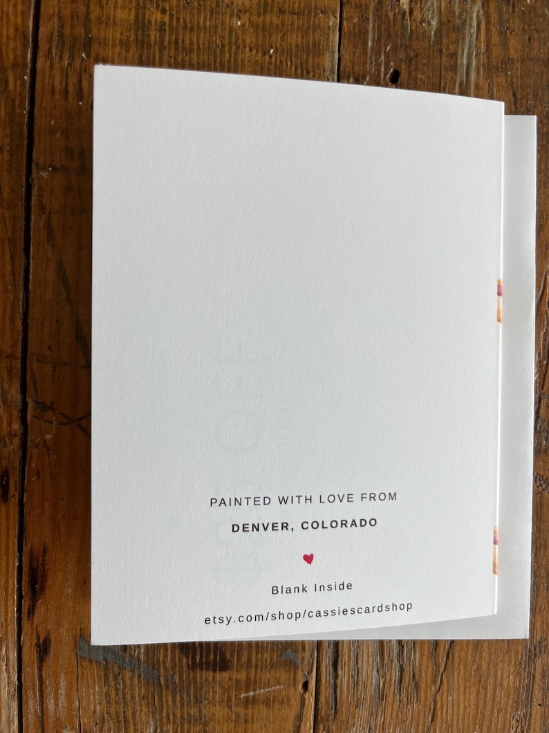 May include: A white greeting card with black text that reads: PAINTED WITH LOVE FROM DENVER, COLORADO, a small red heart icon, the text Blank Inside, and the website address etsy.com/shop/cassiescardshop printed at the bottom center.
