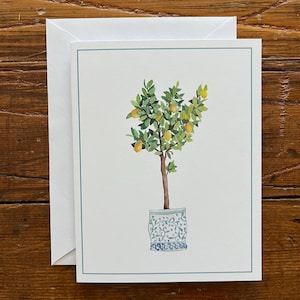 Könnte beinhalten: Aquarell-Grußkarte mit einem Zitronenbaum in einem blau-weiß gemusterten Topf. Der Baum hat grüne Blätter und gelbe Zitronen. Ein weißer Umschlag liegt neben der Karte. Die Karte hat einen hellblauen Rand.