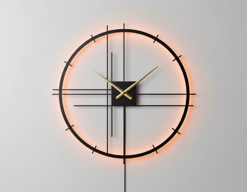 May include: A modern wall clock with a black metal frame and gold-colored hands. The clock features a minimalist design with a circular shape and a warm, orange-colored backlight. The clock's dimensions are not visible.