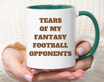Può includere: Una tazza da caffè bianca con un bordo e un manico verdi. La tazza ha un testo marrone che recita "Tears of my Fantasy Football Opponents".