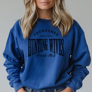 May include: A royal blue sweatshirt with the text "Abandoned Since 2014 Hunting Wives Social Club" printed in black.