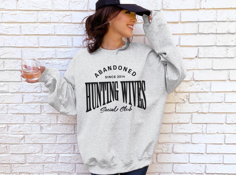 May include: A grey sweatshirt with the text "Abandoned Since 2014 Hunting Wives Social Club" printed on the front.