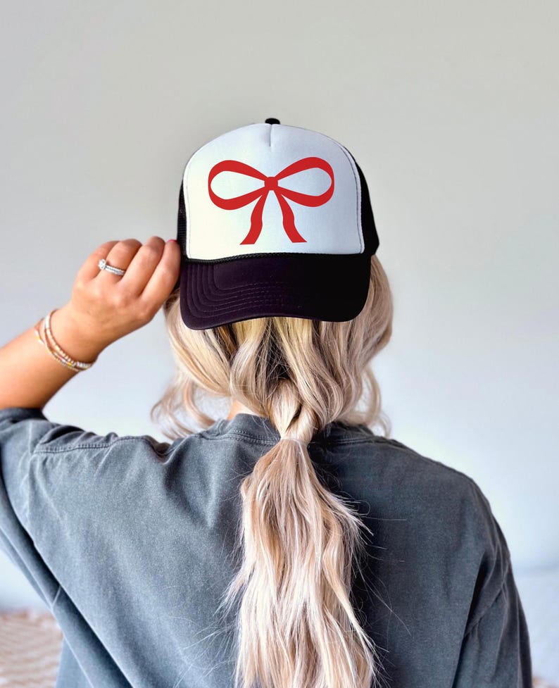 May include: A black and white trucker hat with a red bow on the front. The hat has a mesh back.