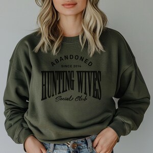 May include: A green sweatshirt with the text "Abandoned Since 2014 Hunting Wives Social Club" printed on the front.