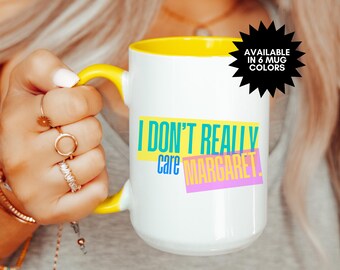 May include: White ceramic mug with a yellow rim and handle. The mug has the text "I don't really care Margaret." printed in colorful letters.