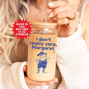 Peut inclure: Un gobelet en verre de 473 ml avec un couvercle en bambou et un motif de grenouille. Le gobelet porte l'inscription "I don't really care, Margaret".