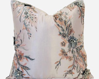 May include: A decorative throw pillow with a light pink background and floral embroidery in shades of gray, pink, and brown. The embroidery features delicate flowers and leaves with beaded accents.