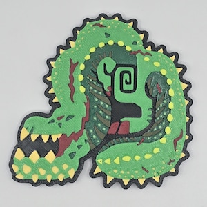May include: Green and yellow 3D printed patch of a crocodile with a spiral design on its back.
