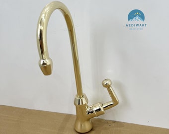 May include: A gold-colored faucet with a curved spout and a single lever handle. The faucet is made of brass and has a polished finish. The brand name "AZDIWART BRASS PURE" is printed on the white background.
