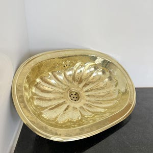 May include: A large, oval-shaped brass sink with a hammered finish. The sink has a flower-like design with a drain in the centre.