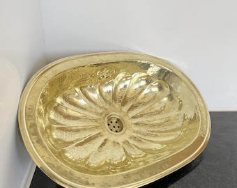May include: A large, oval-shaped brass sink with a hammered finish. The sink has a flower-like design with a drain in the center.