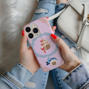 May include: A pink iPhone case with a floral design and a cartoon image of a woman wearing a crown and a dress. The case has a cutout for the camera lens.