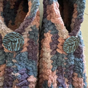 May include: A pair of fuzzy slippers with a pink, blue, and purple color scheme. Each slipper has a round button with a zebra print design.